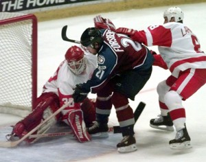 Colorado Avalanche center Peter Forsberg (21) slips past the defense of Detroit Red Wings goalie Chris Osgood, left, and center Igor Larionov for the Avalanche's fifth goal during the third period in Game 6 of the Western Conference semifinals in Detroit, Tuesday, May 18, 1999. The Avalanche defeated the Red Wings 5-2 to advance to the finals. (AP Photo/Carlos Osorio)